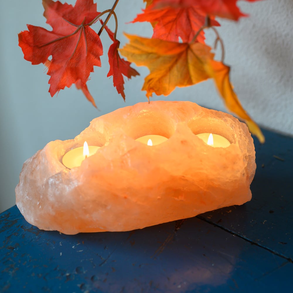Saltlampa Stearinljushållare med tre ljus. Blått bord med dekorativa löv i bakgrunden